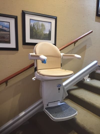 Straight stairlift with cream-colored upholstery on carpeted stairs